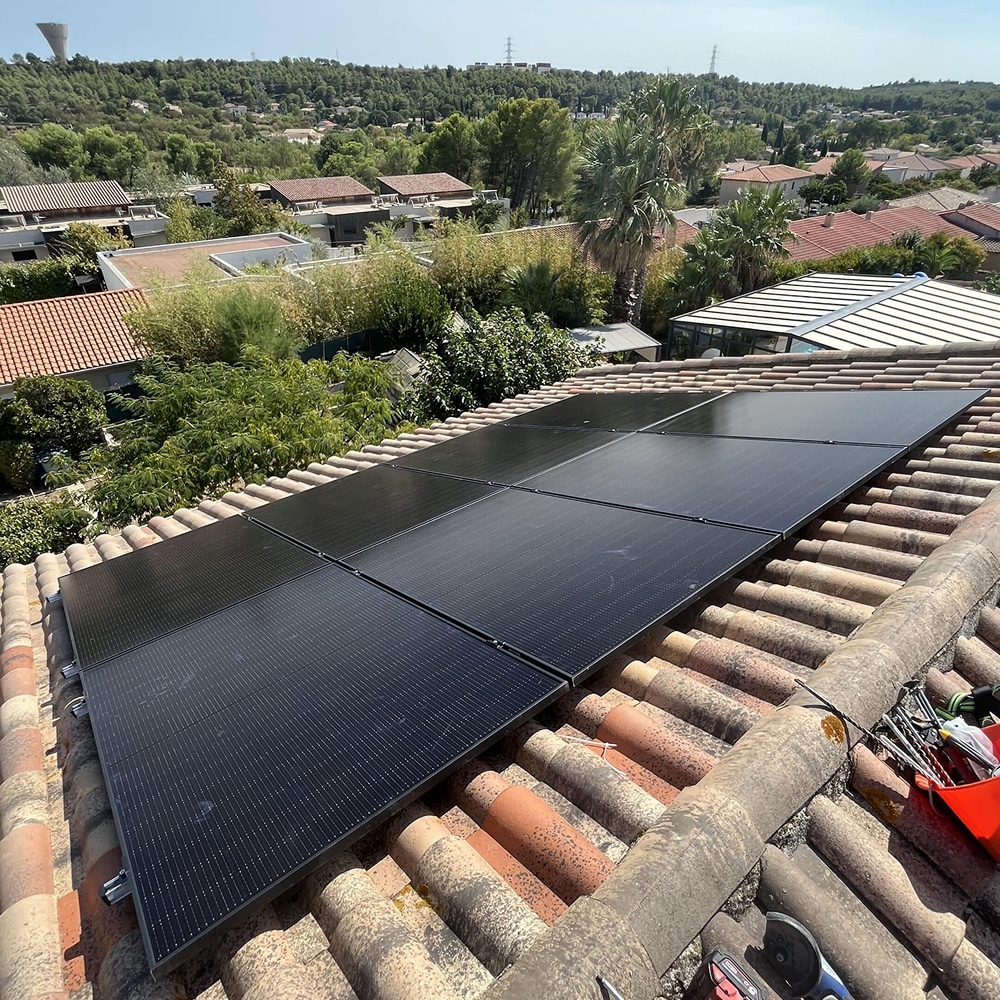 Panneaux solaires photovoltaïques noirs installés sur un toit en tuiles romanes avec vue sur un paysage boisé.